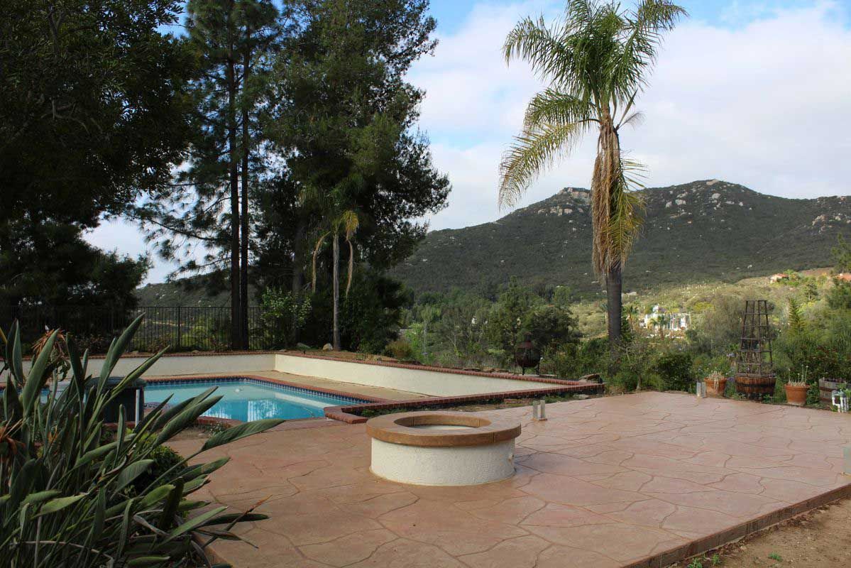 Backyard patio with swimming pool, palm trees, and mountain view at sunset