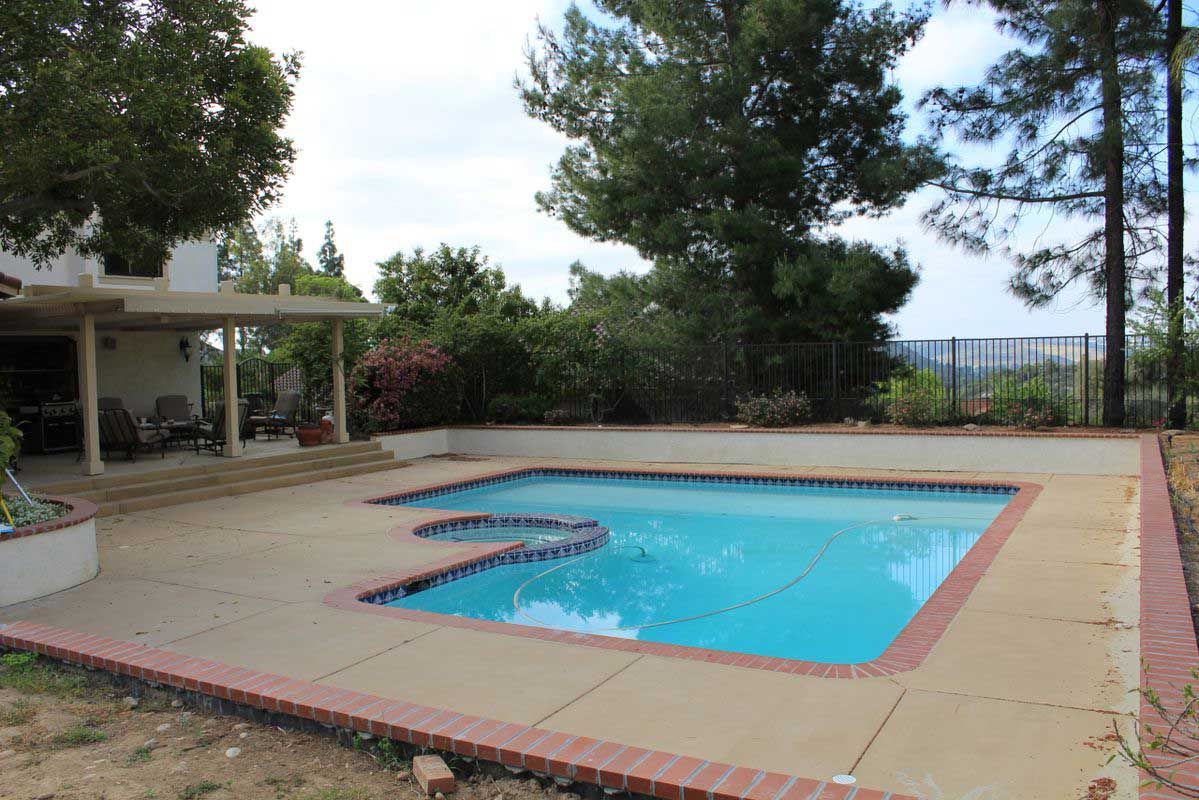 Outdoor backyard swimming pool with patio, trees, and a covered seating area