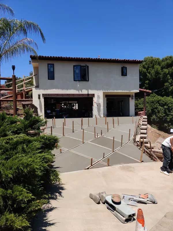 House under construction with a concrete driveway and wooden form stakes in front, under a clear blue sky