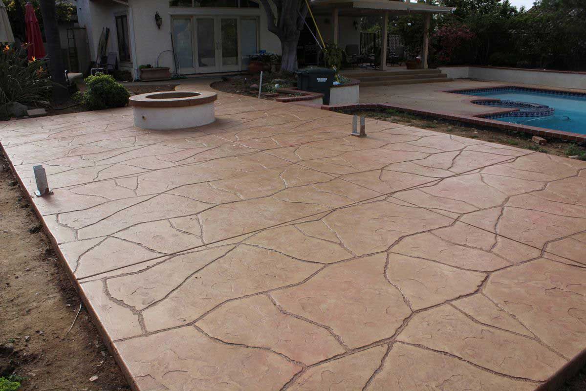 Patio with stamped concrete, round fire pit, and swimming pool beside a house.