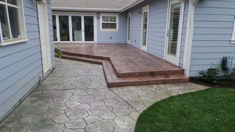 Backyard patio with stone pavers, raised wooden deck, and light blue house siding