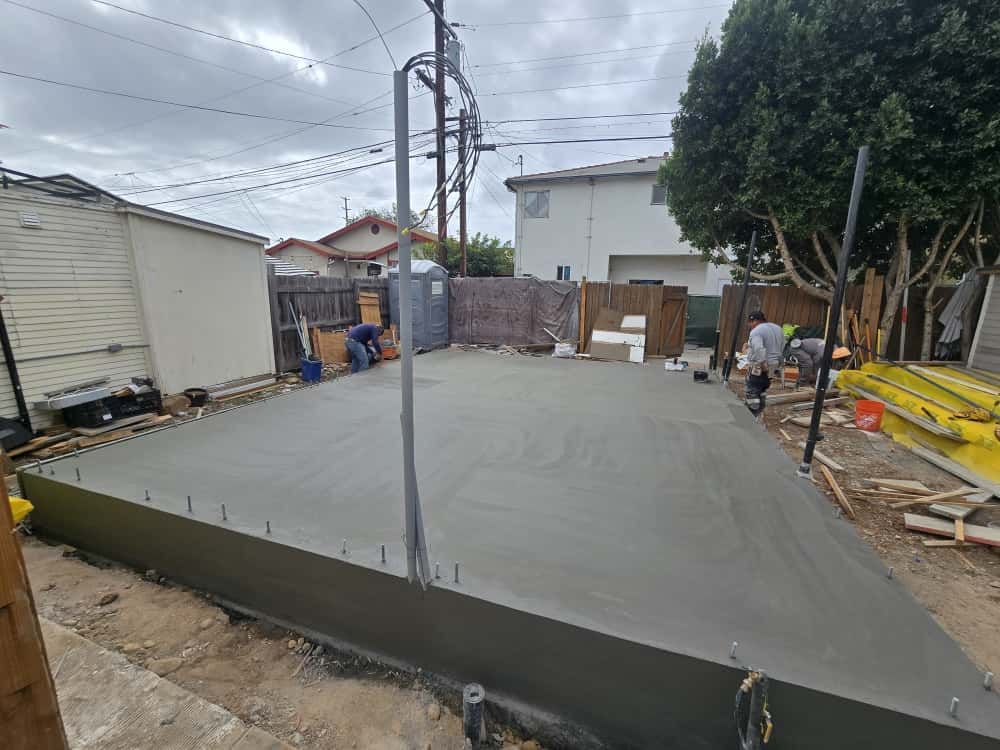 Fresh concrete slab poured in a narrow outdoor alley with workers and construction materials nearby