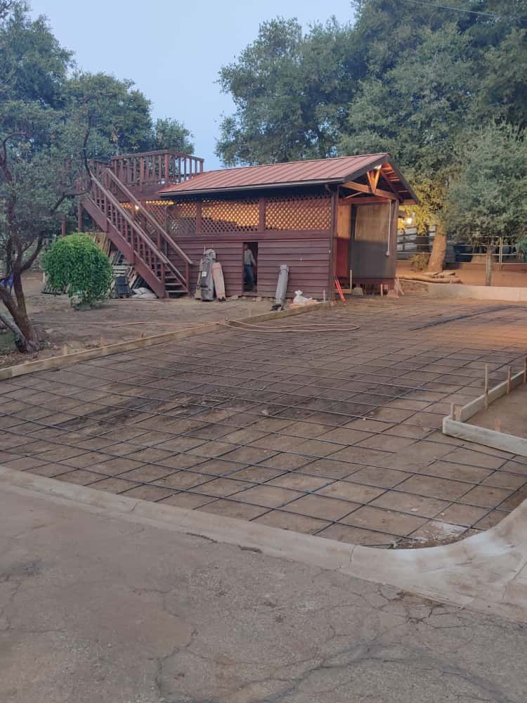 Small wooden building with an exterior staircase beside a paved courtyard and trees.