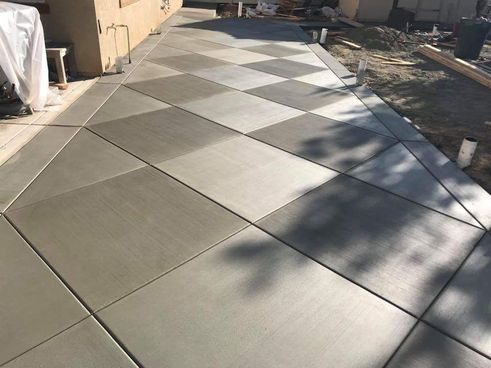 Diagonal gray and light-gray tiled walkway beside a building, with tree shadows across the path