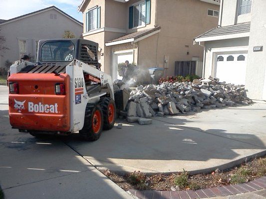 Bobcat loader beside a pile of broken concrete in a suburban driveway