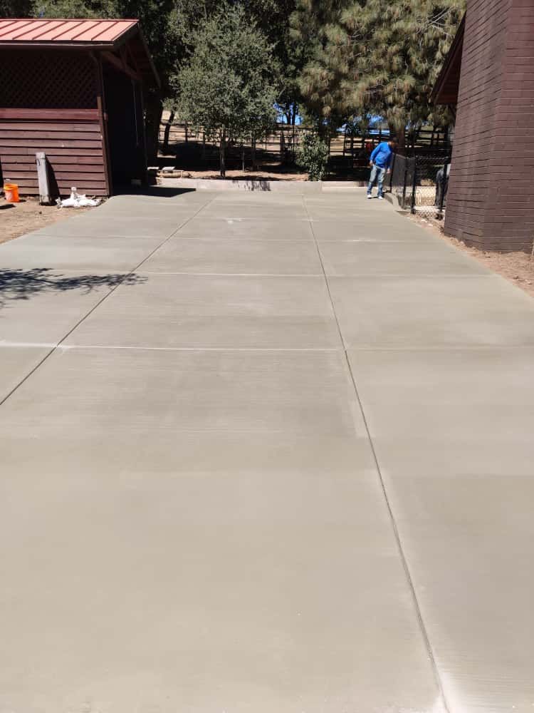 Concrete walkway between brick buildings with two people in blue shirts in the distance, trees ahead