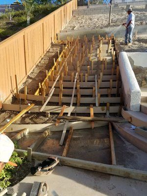 Construction site with wooden forms and rebar for a concrete stairway beside a fence