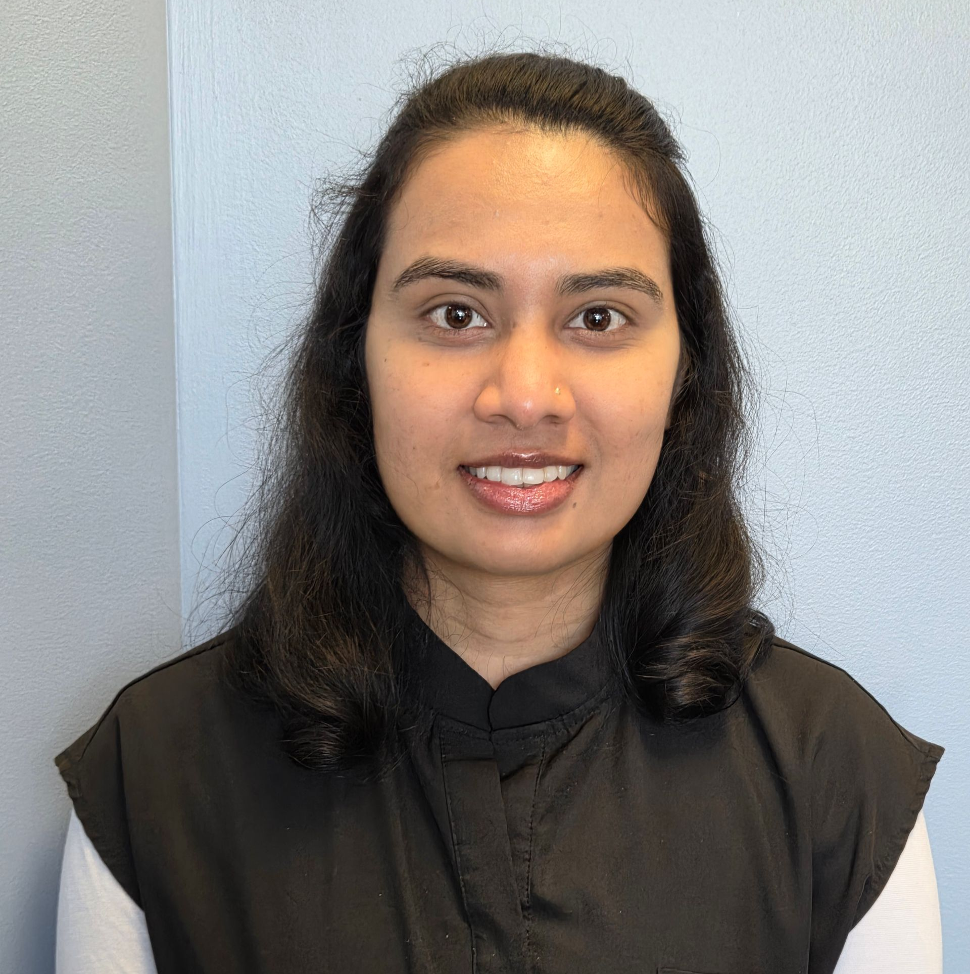 A woman wearing glasses and a blue scrub is smiling for the camera.