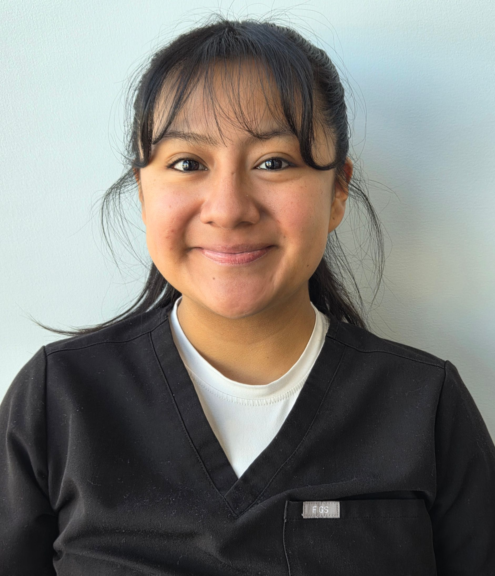 A woman wearing glasses and a blue scrub top is smiling for the camera.