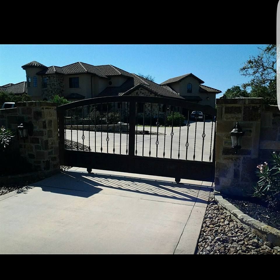 Black metal gate blocking a driveway in front of a large house on a sunny day