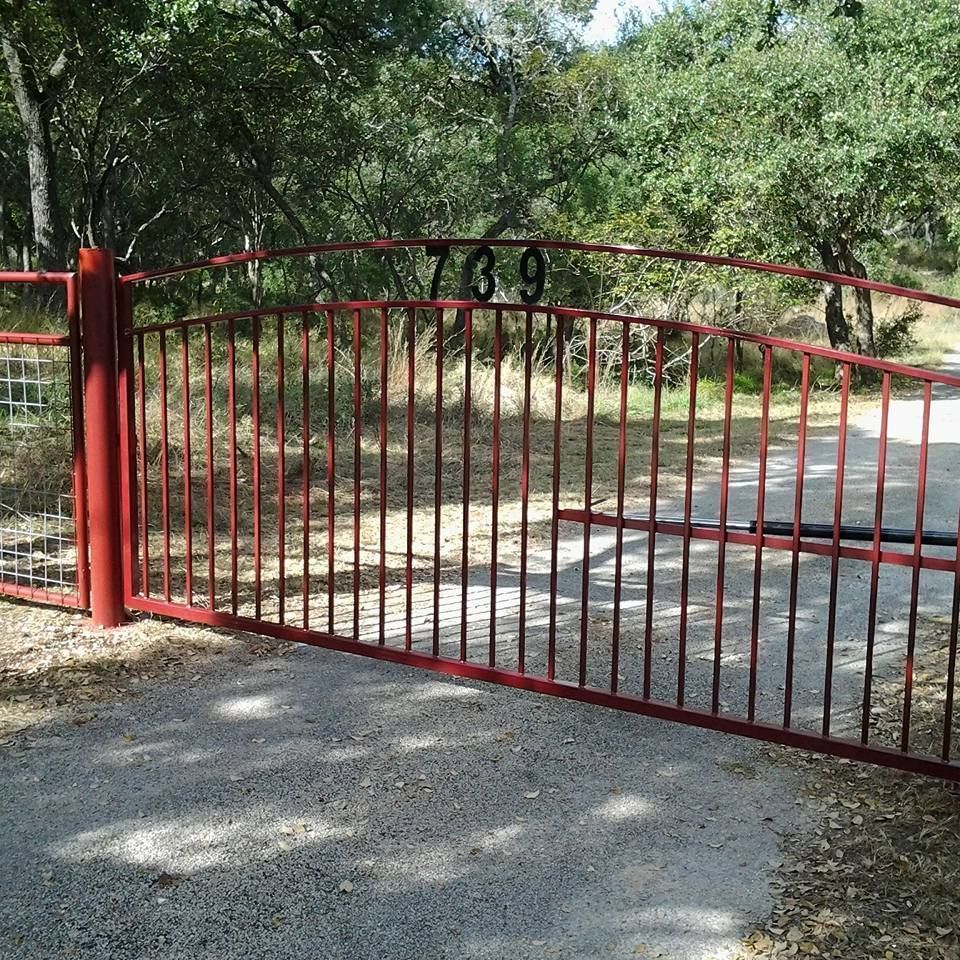 Red metal gate blocking a paved driveway at the entrance to a wooded property