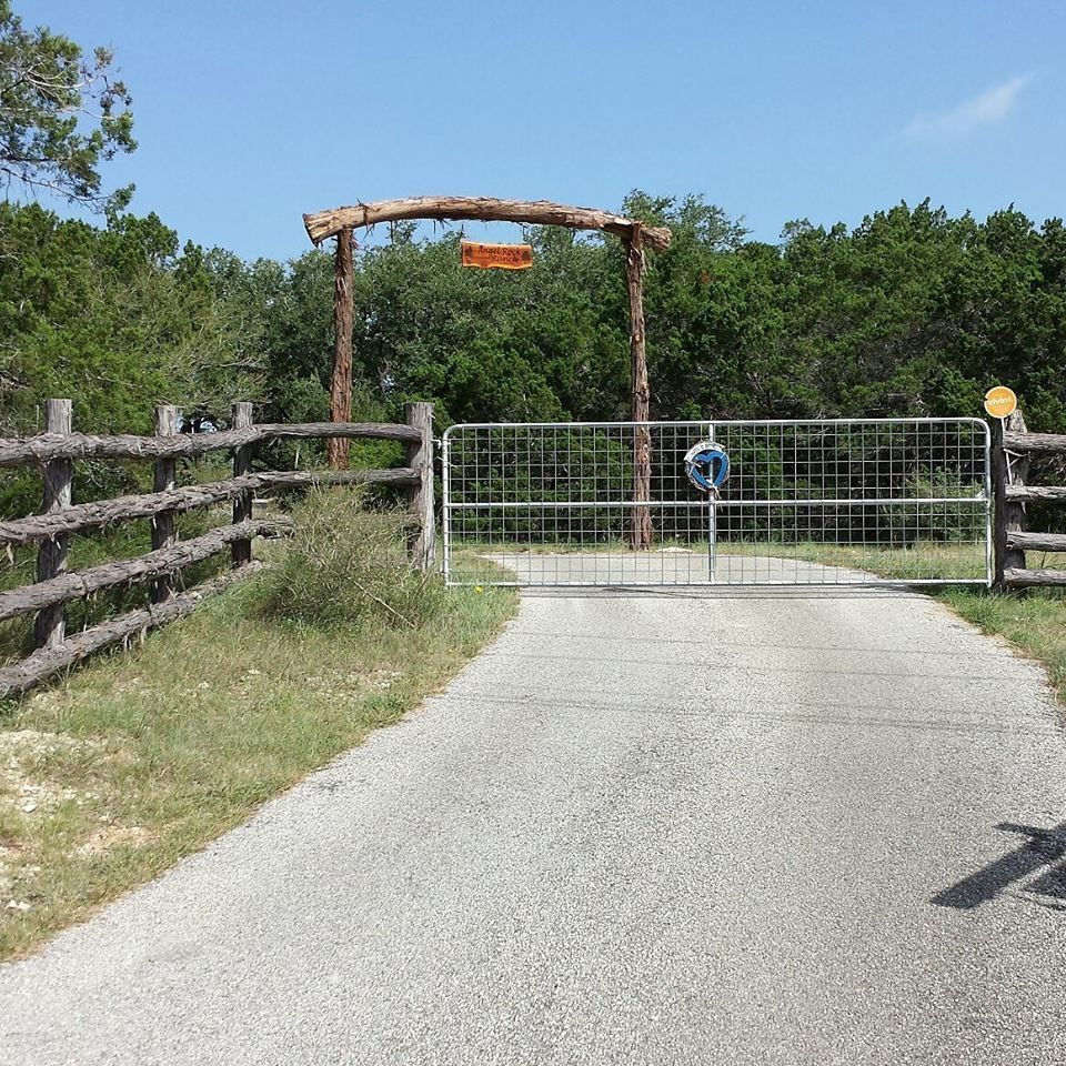 Closed gate blocking a paved trail, with wooden fencing and trees under a clear sky