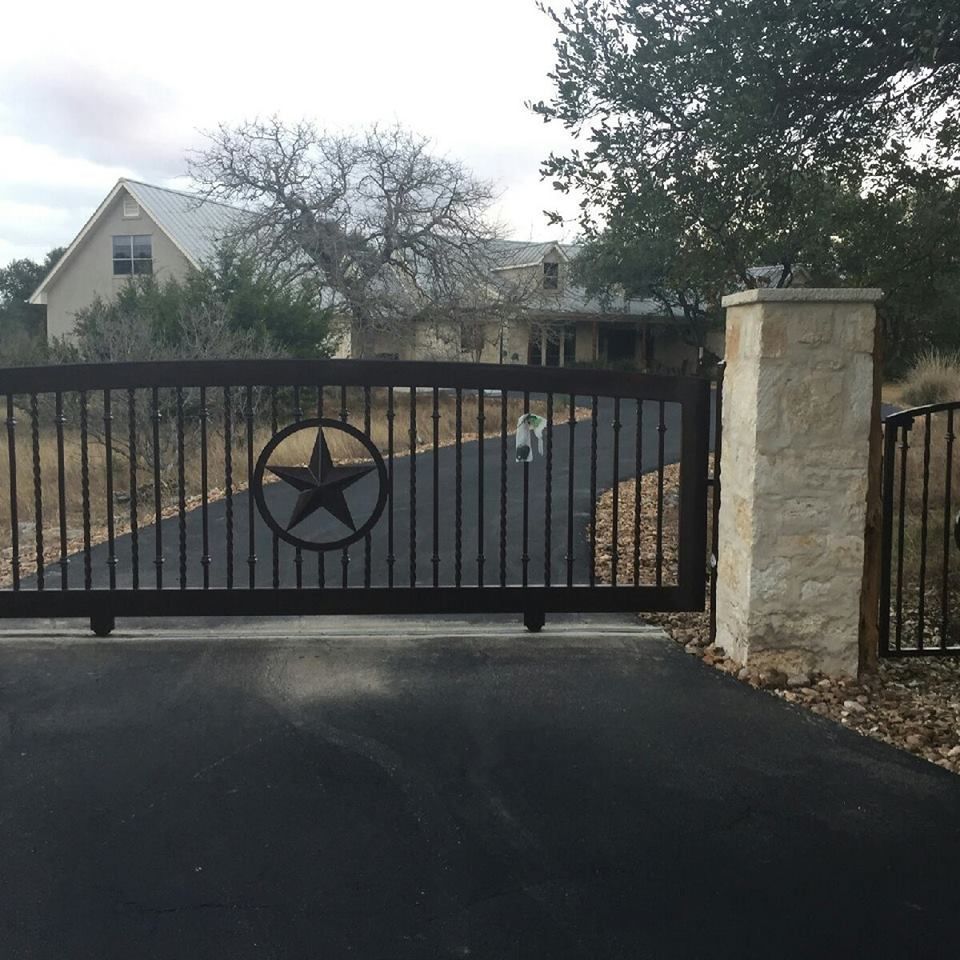 Black driveway gate with star emblem, stone pillars, and a house in the background