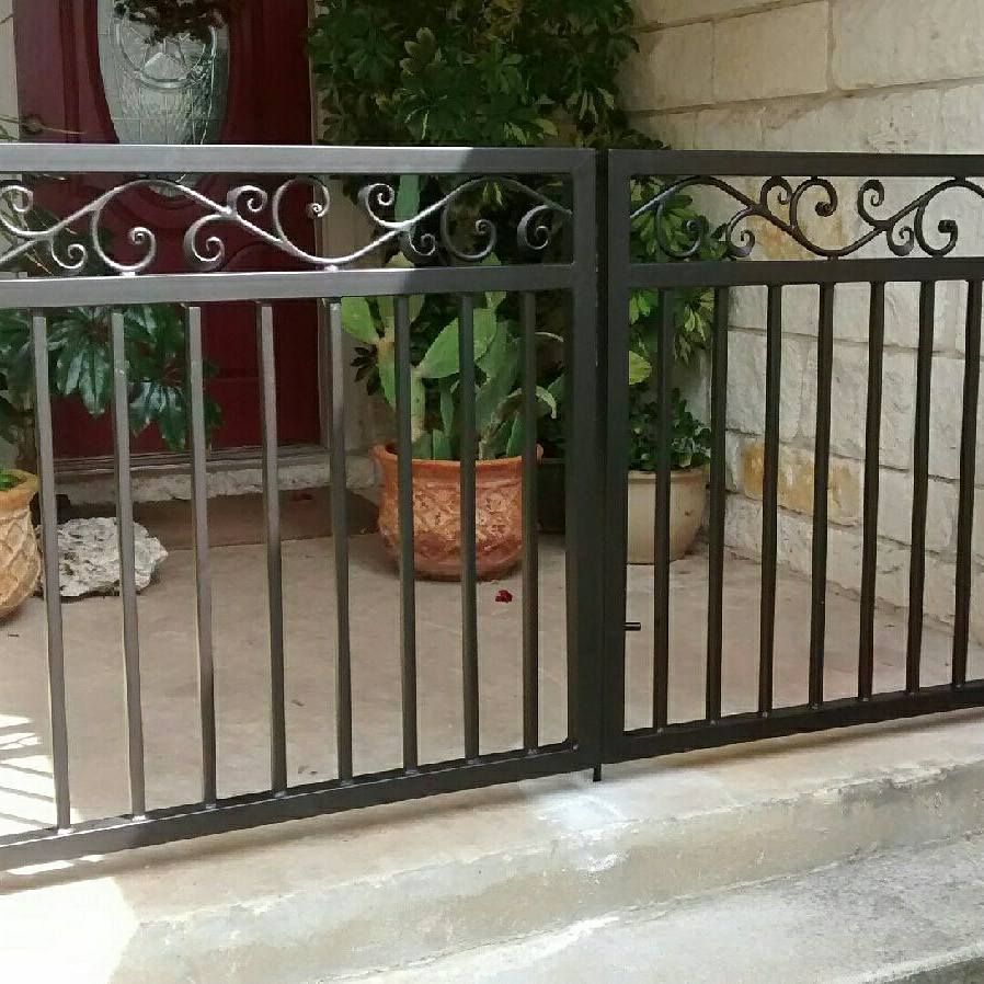 Black metal gate with decorative scrollwork in front of a courtyard with potted plants.