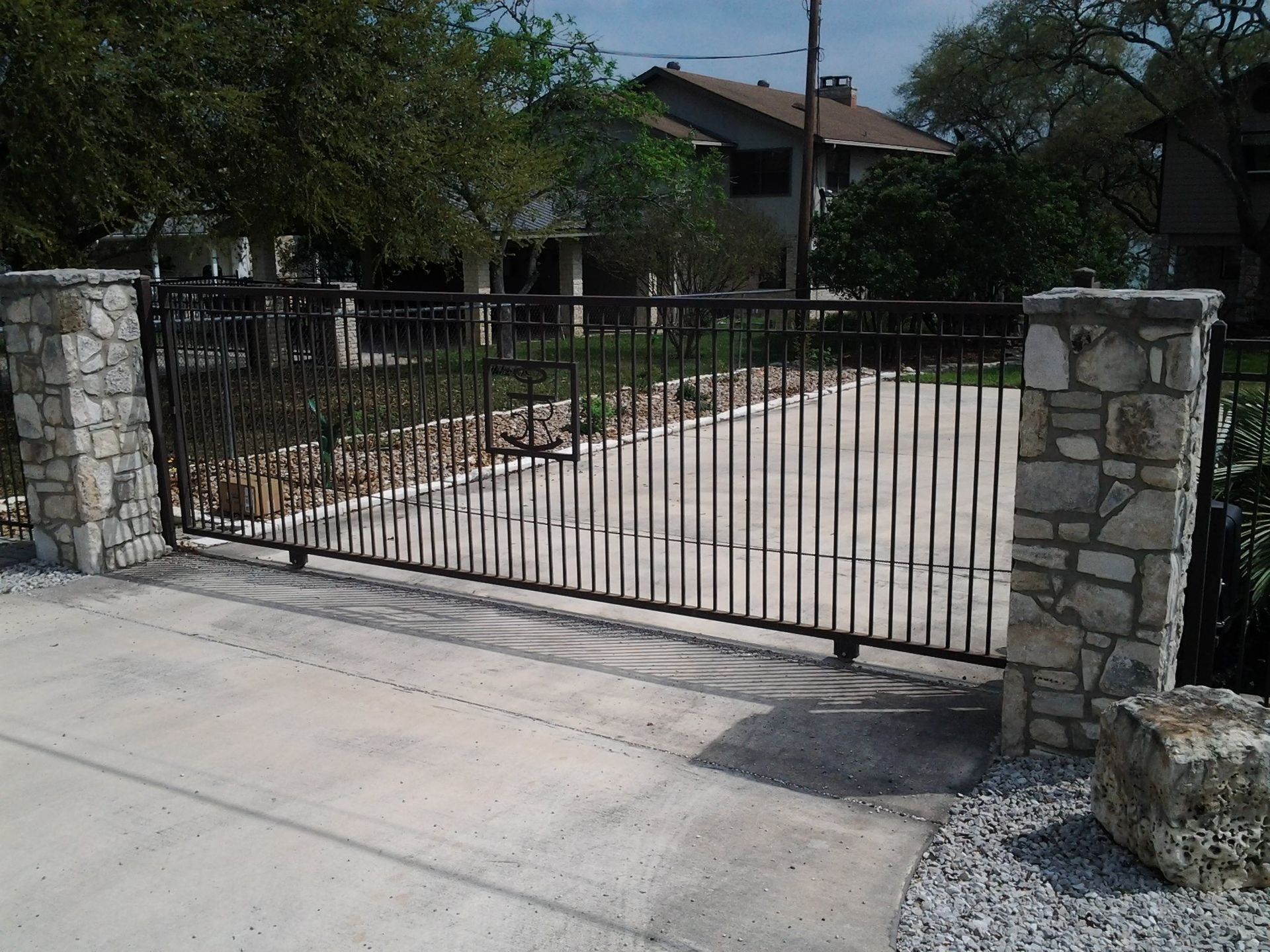 Black iron driveway gate between stone pillars at a residential entrance.