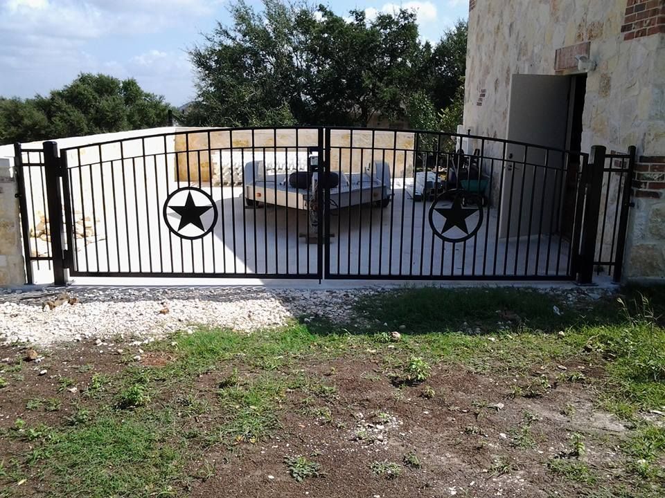 Black metal gate with star emblems in front of a patio and pool area beside a stone house