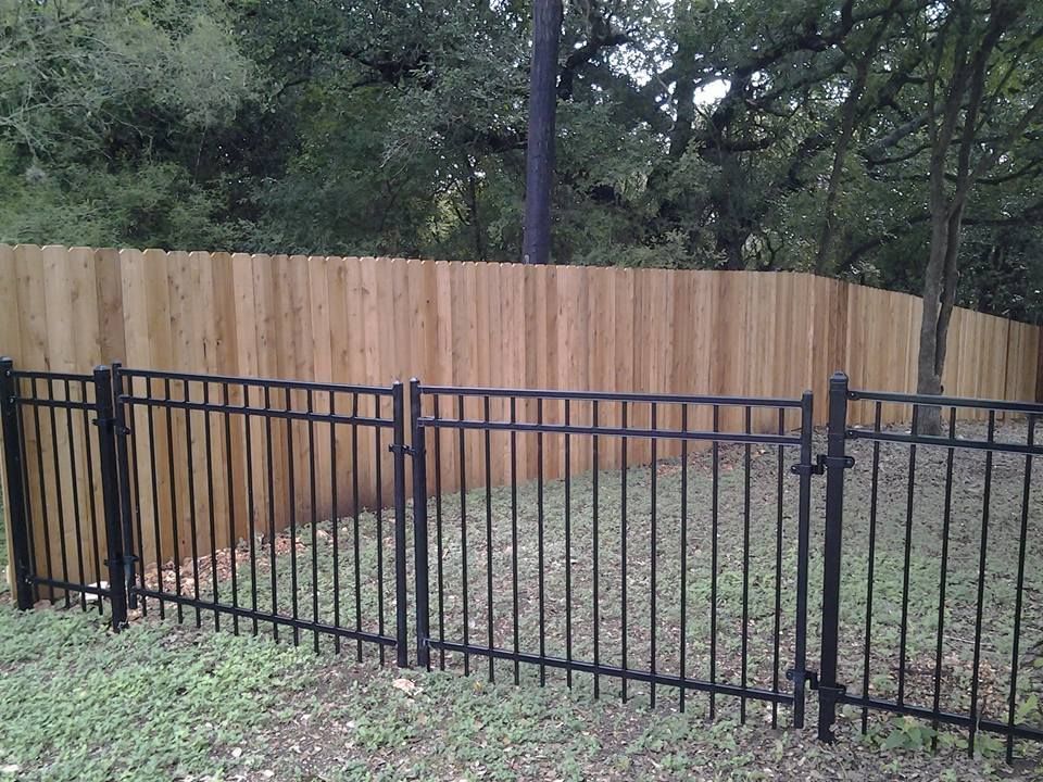 Black metal fence in front of a wooden privacy fence in a grassy yard with trees behind it