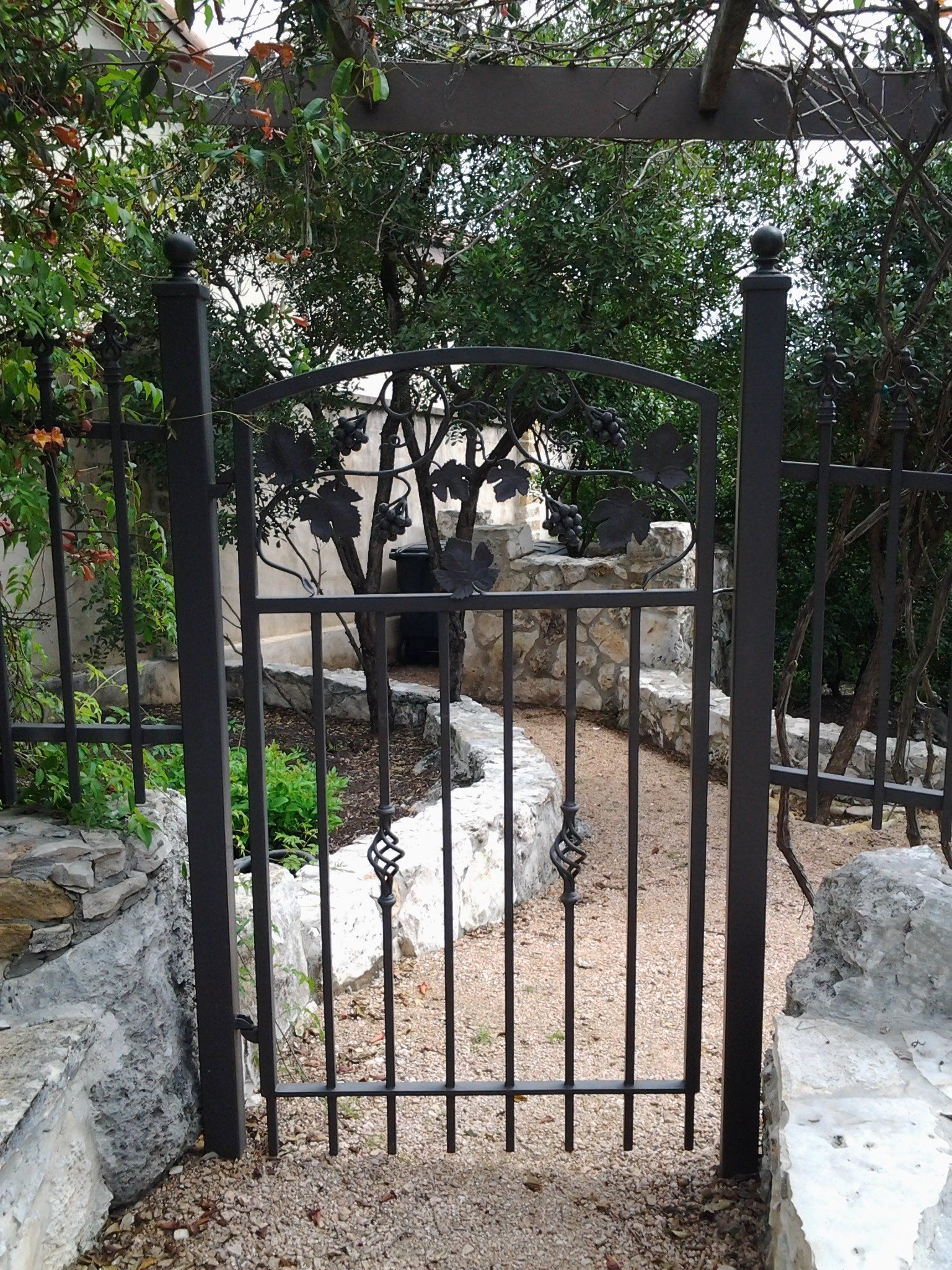 Iron gate leading to a garden path between stone walls and greenery
