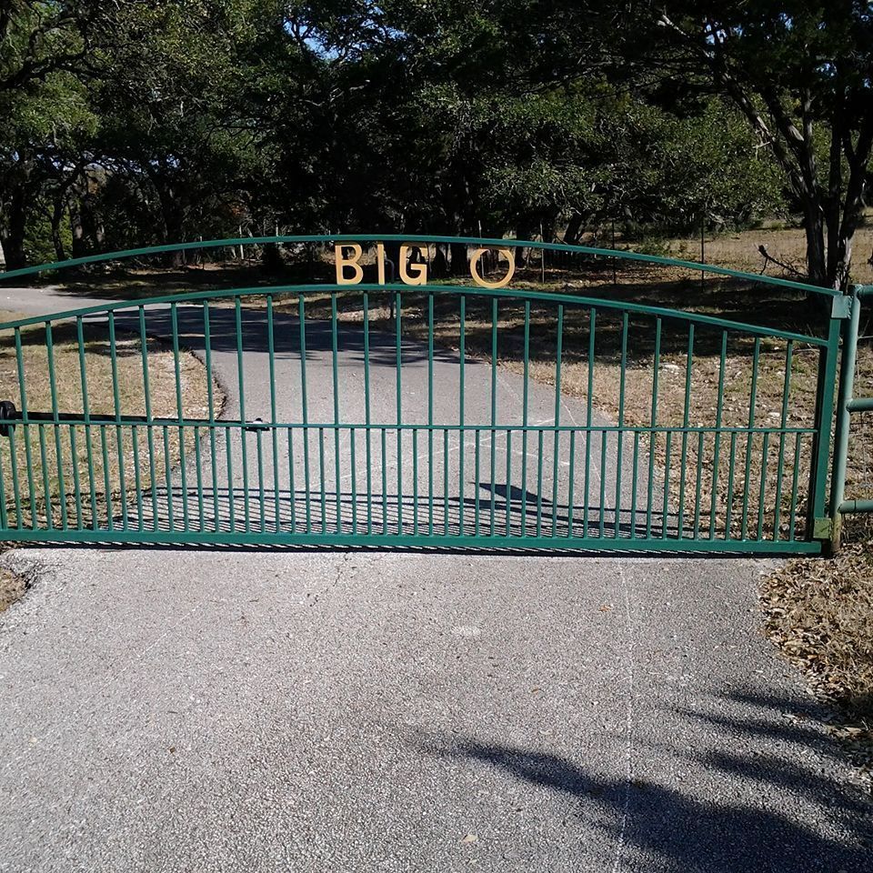 Green metal gate across a driveway with “BIG O” lettering, viewed from the road