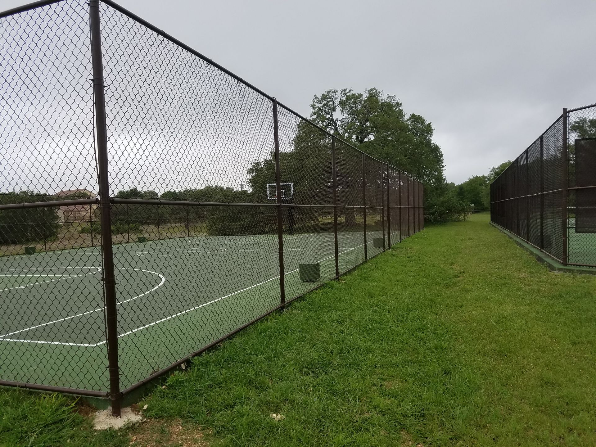 Empty fenced outdoor sports court beside a grassy path under cloudy skies