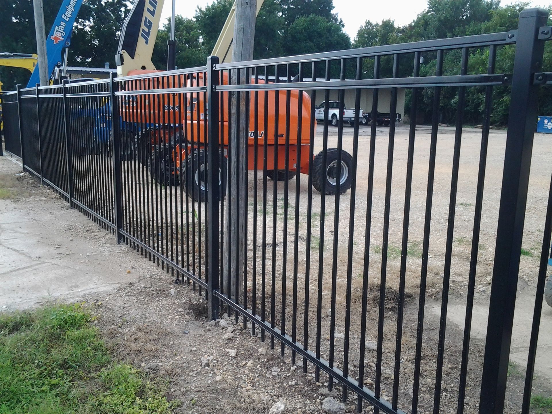 Black metal fence beside a construction site with orange lift equipment and dirt ground