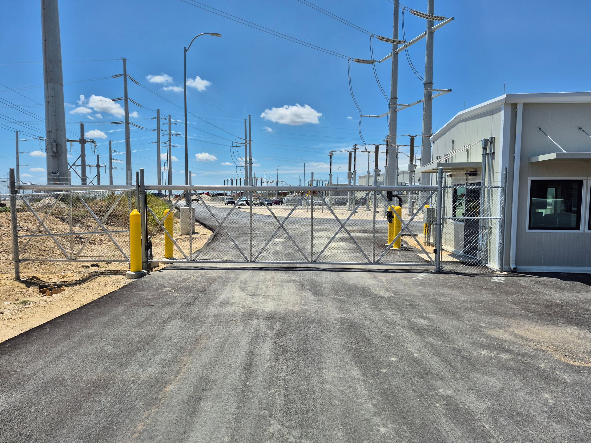 Closed metal gate at an industrial facility entrance on a paved road under a blue sky