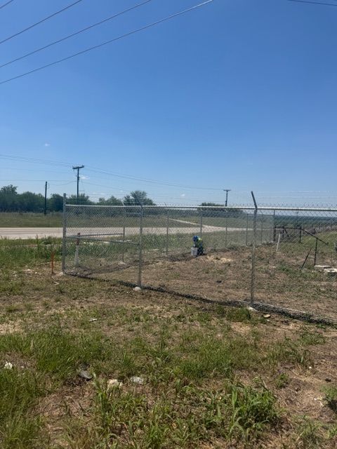 Chain-link fence and gate in a dry field under a clear blue sky.