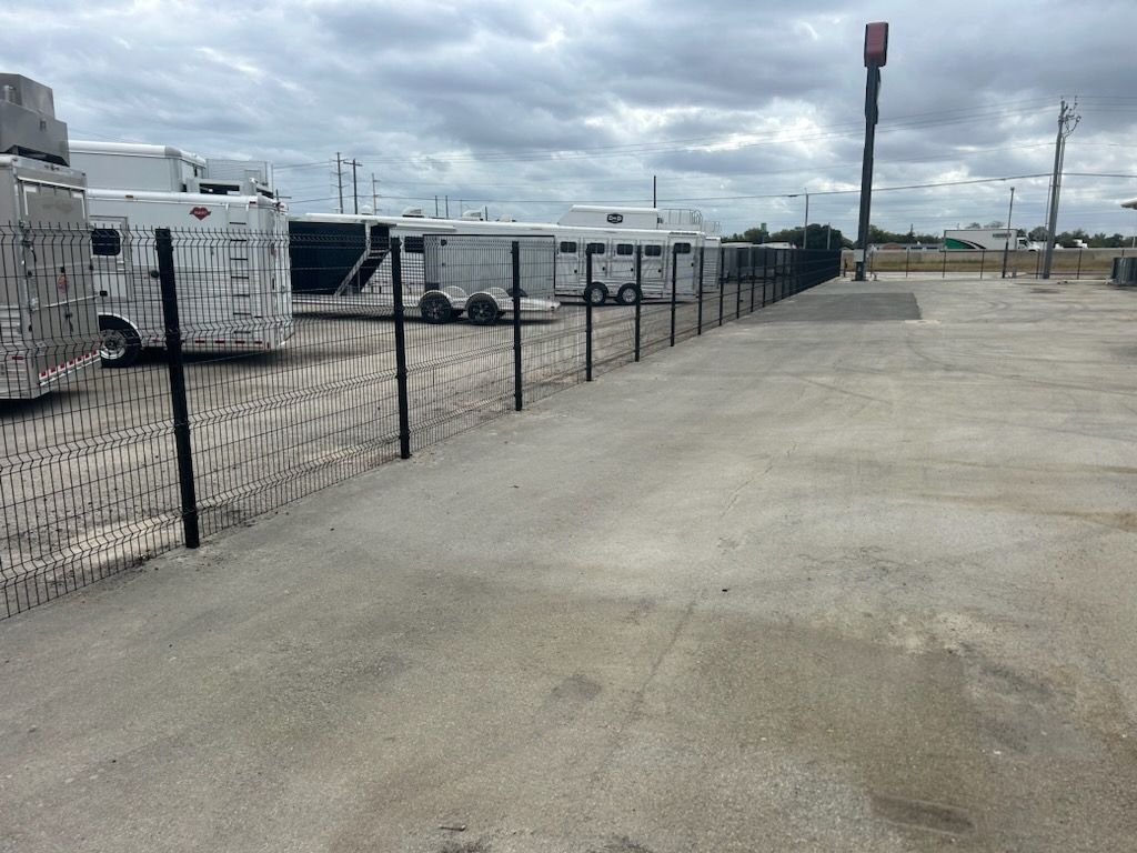 Industrial yard with chain-link fence, stacked pallets, and a wide concrete lot under cloudy skies