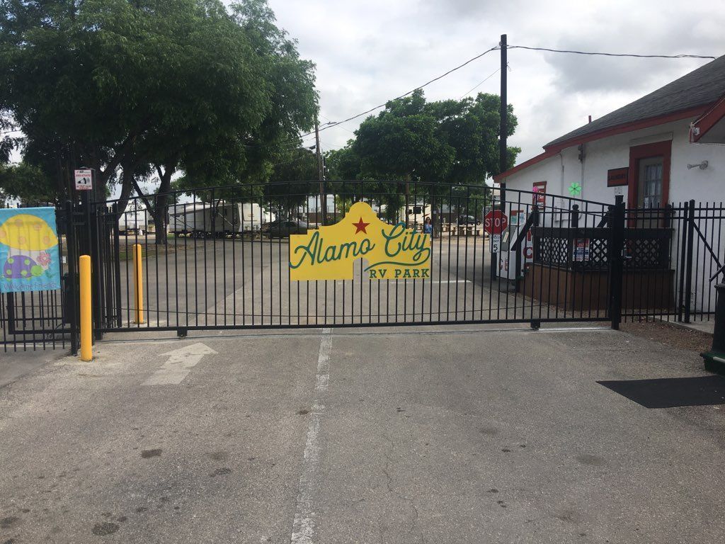 Gated entrance to a building with a yellow “Mami’s” sign, trees, and a cloudy sky.
