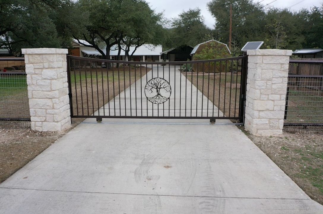 Closed wrought-iron driveway gate between stone pillars at the end of a concrete drive