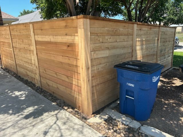 Wooden privacy fence along a sidewalk with a blue recycling bin in front