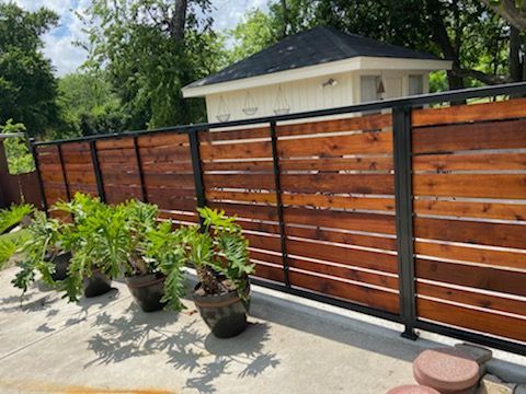 Wooden privacy fence with black posts beside potted plants on a concrete patio in a backyard