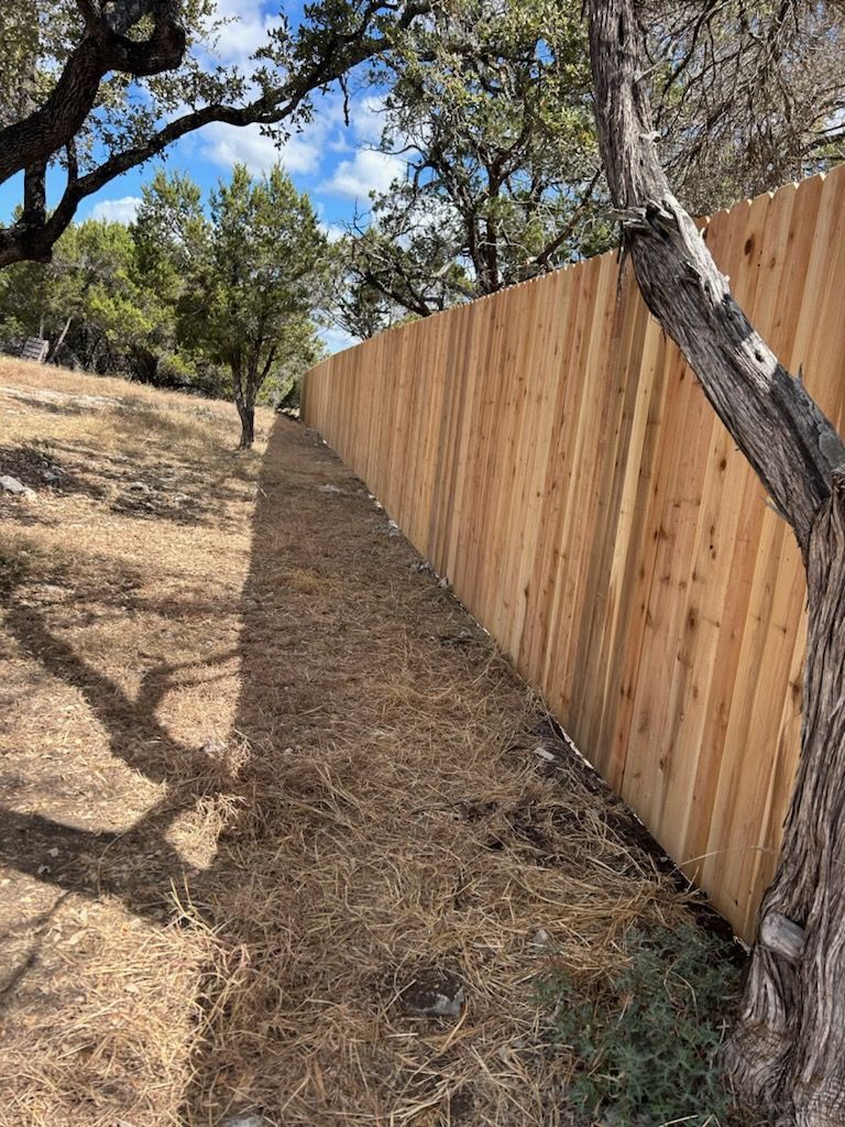 Wooden fence along a dry hillside with oak trees and blue sky