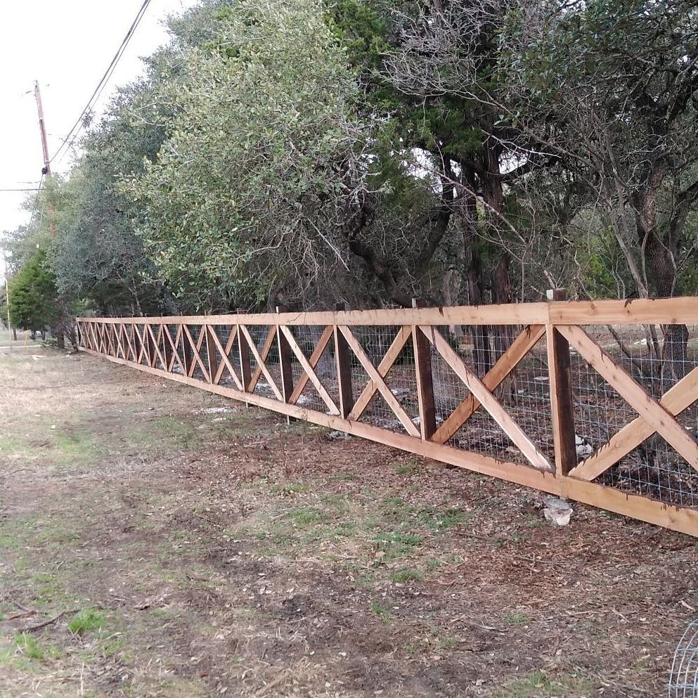 Wooden fence with diagonal cross-bracing along a grassy roadside beside trees