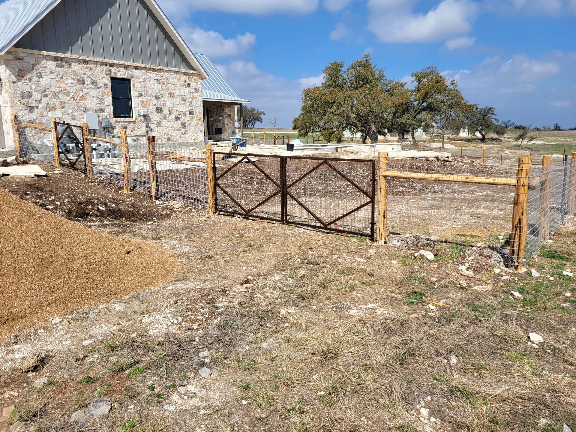 Rustic stone house with a wooden gate and fenced yard under a blue sky