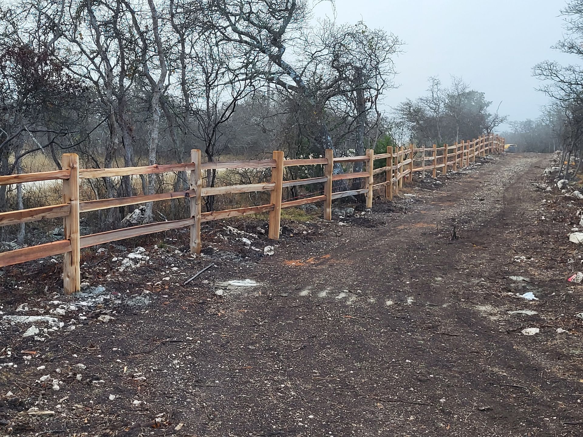 Wooden fence lining a muddy dirt path through a misty wooded area