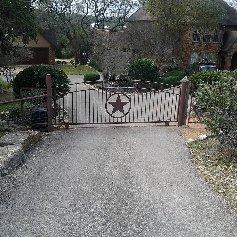 Driveway leading to a metal gate with a star emblem in front of a house and trees