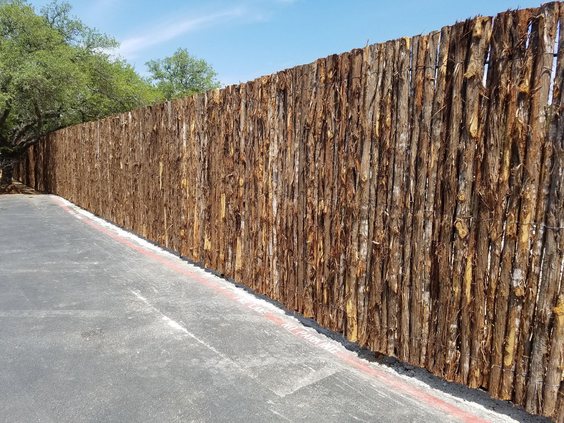 Rustic wooden fence along a paved road under a clear blue sky