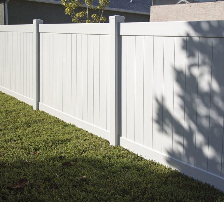 White vinyl fence along a grassy yard in sunlight, with tree shadows on the panels