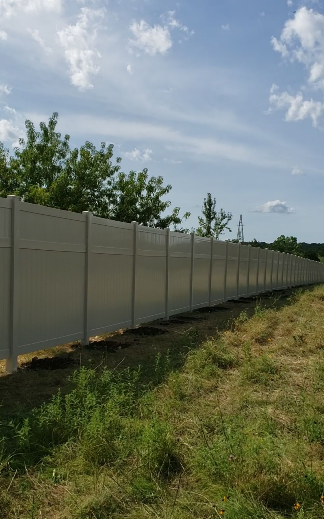 Long white fence along a grassy field under a partly cloudy sky
