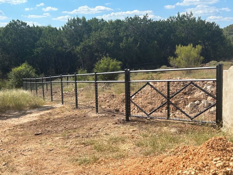 Rural fenced gate along a dirt path, with trees and blue sky in the background.