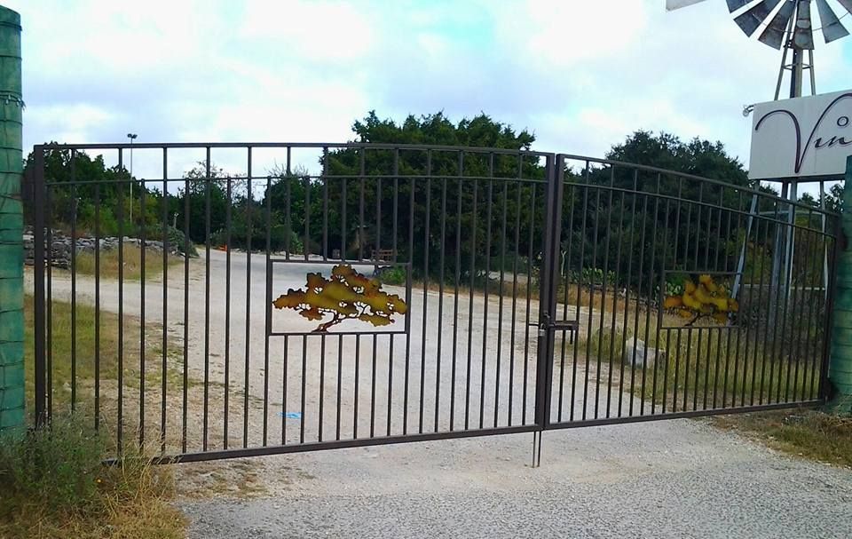 Closed metal gate across a gravel driveway with a windmill and trees behind it