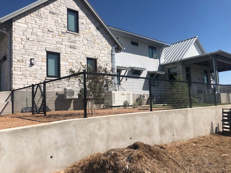 Stone house with black fence and metal-roofed porch on a sloped yard under a blue sky