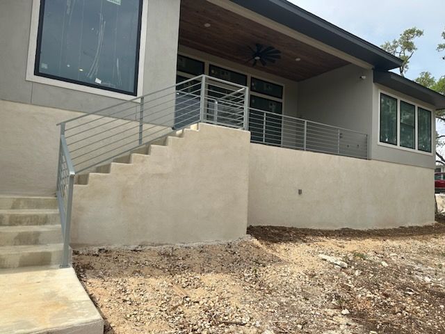 Modern house exterior with front steps, metal railings, and a dirt yard.