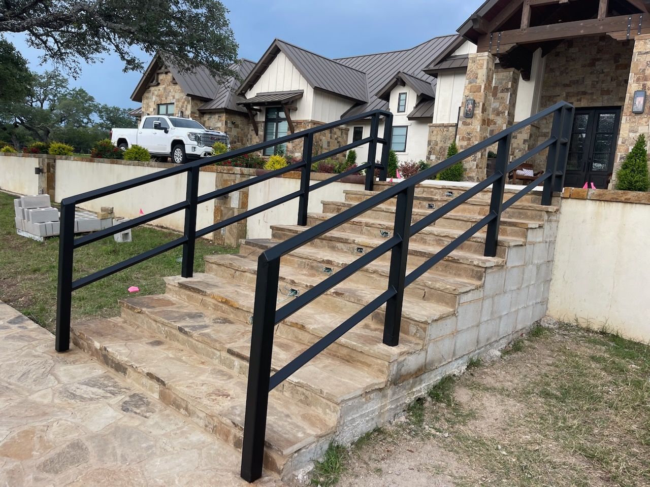 Stone steps with black handrails leading to a house entrance in a suburban neighborhood
