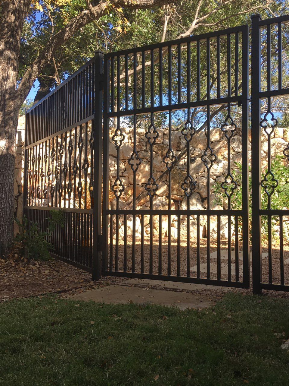 Black iron gate in a leafy outdoor area with trees and grass nearby