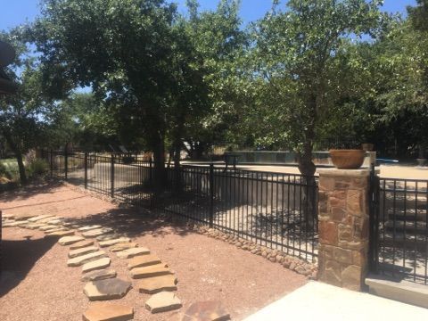 Stone path beside black metal fence and stone pillars in a sunny backyard garden