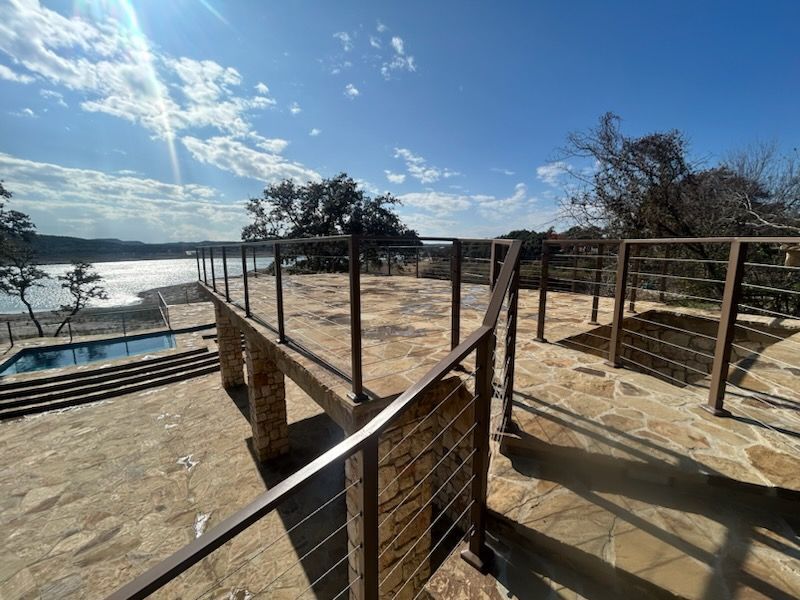 Stone riverside terrace with metal railings overlooking a lake under a bright blue sky