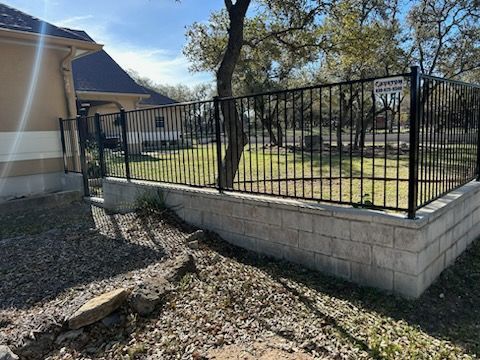 Black metal fence on a raised concrete wall beside a house and yard