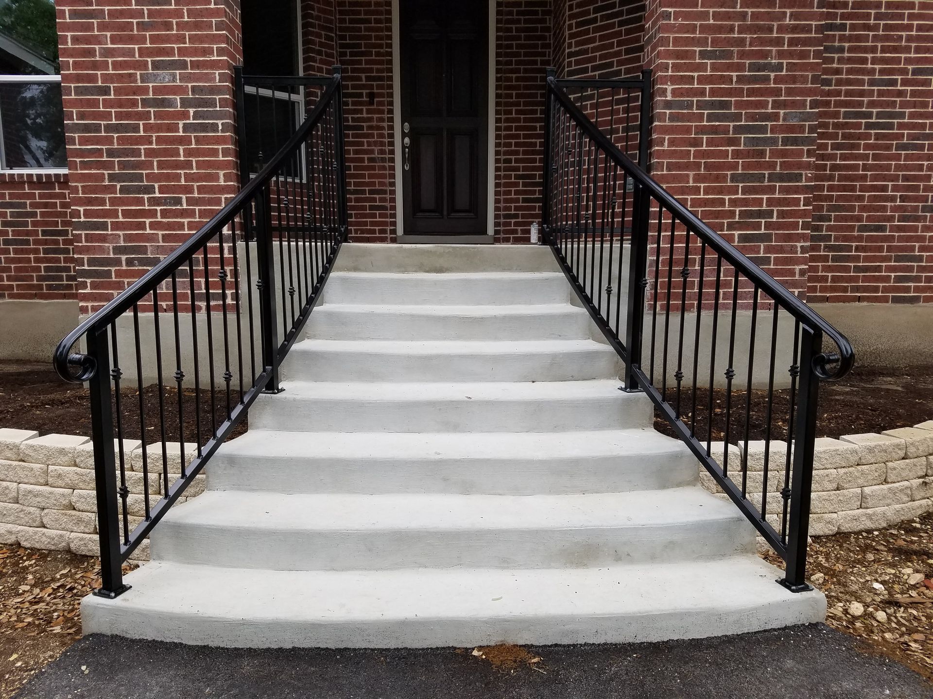 Brick building entrance with curved concrete steps and black metal railings